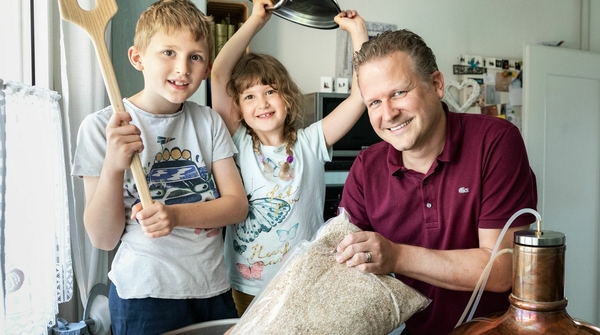 Ein Mann mit seinen beiden Kindern, ein Junge und eine Mädchen, brauen Bier in einer Küche.