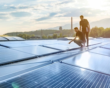 Zwei Monteure stehen auf einem Dach mit montierten PV-Anlagen.