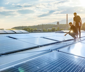 Zwei Monteure stehen auf einem Dach mit montierten PV-Anlagen.